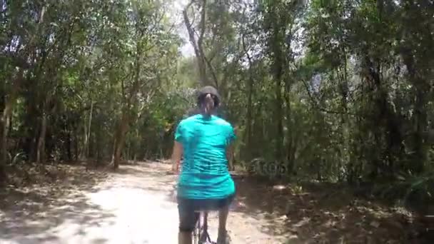 Una mujer montando una bicicleta por un sendero de la selva — Vídeos de Stock