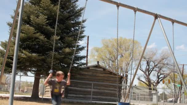 Niño en columpios en el parque público — Vídeos de Stock