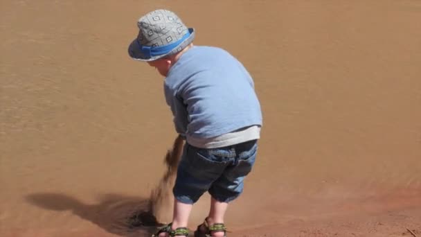 Junge schüttet Sand aus Eimer in Fluss — Stockvideo