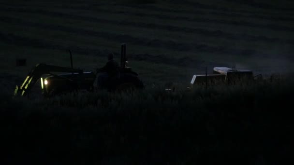 Фермер сбрасывает сено поздно вечером — стоковое видео