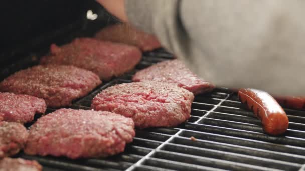 Man kruiden hamburgers en hotdogs op grill — Stockvideo