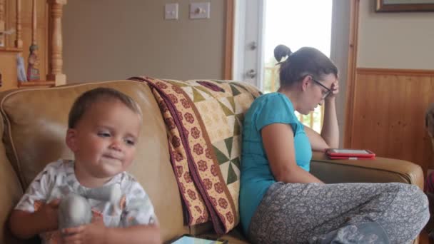 Мама читает электронную книгу, пока малыш играет на iPad — стоковое видео
