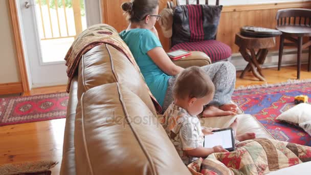 Matka czyta ebook, podczas gdy malucha odgrywa na ipad — Wideo stockowe