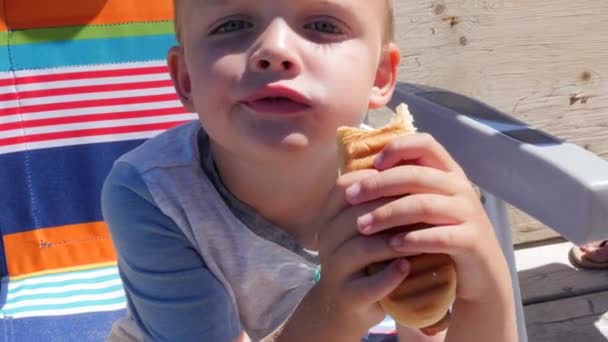 Ένα Αγόρι Φαγητό Ενός Hotdog Στο Boardwalk Από Τον Ωκεανό — Αρχείο Βίντεο