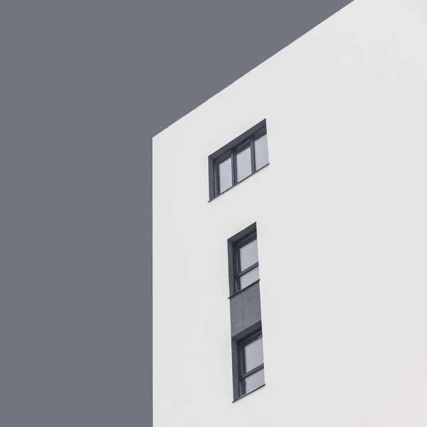 White apartment block with dark grey windows under abstract grey sky. Isolated. Quadrate photo. Bottom view. Concept: life, couple, family, kids, independence, abstract, minimalism. — Stock Photo, Image