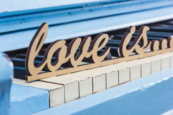 Синий пианино крупным планом с черно-белыми клавишами с текстом Love is — стоковое фото