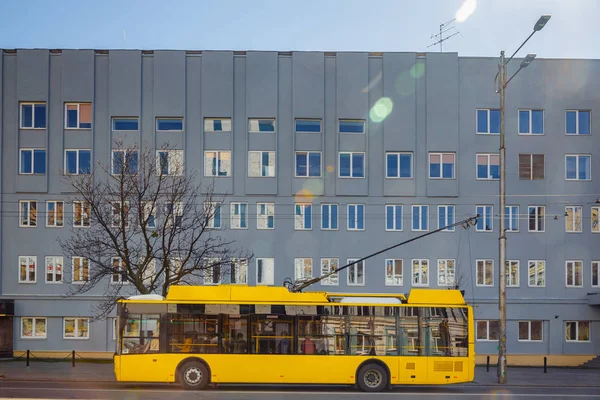 A yellow trolleybus is standing at a bus stop near the big house Stock Photo