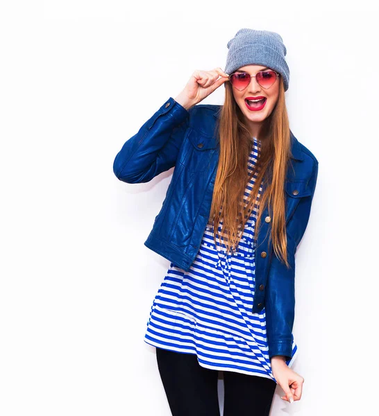 Hermosa chica hipster sexy joven posando y sonriendo cerca de blanco wall.Street stylehipster look.wearing chaqueta de cuero azul, vestido a rayas, sombrero gris. . — Foto de Stock