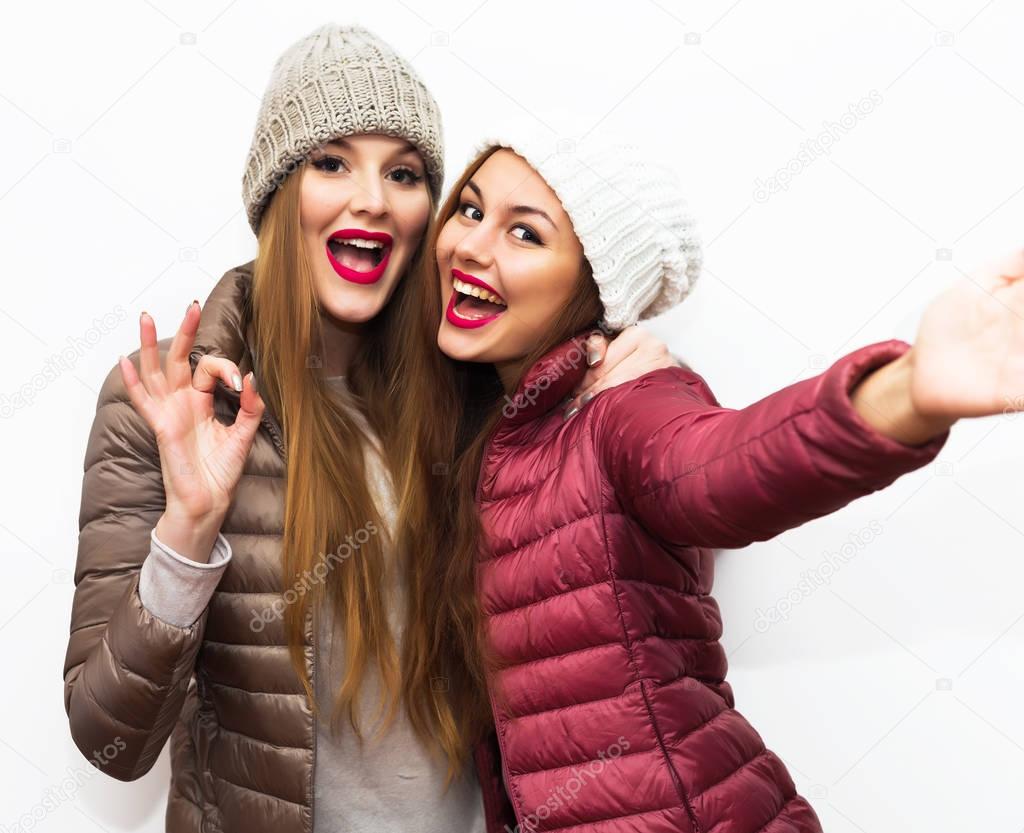 Stock Photo: Close up lifestyle selfie portrait of pretty fresh young brunette and blonde best friends girls making selfie,having fun,smiling,showing ok,wearing winter coats and hats. Fresh make-up.Stock Photo: Close up lifestyle selfie portrait of p