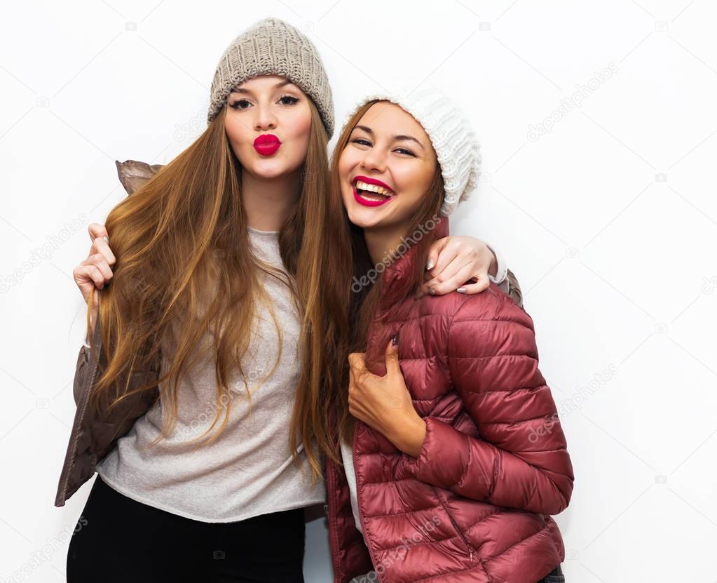 Indoor fashion lifestyle portrait of two young girl friends standing together and having fun. Looking at camera.Having fun together and sending kisses.