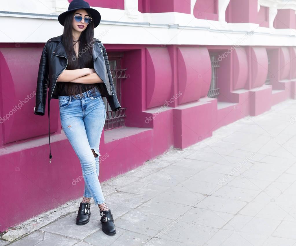 Outdoor fashion portrait of stylish sexy woman, stylish outfit,wide hat,jeans and leather jacket, bright fashion details, positive mood.Street style in Europe city center.