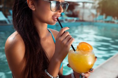 Havuzu, yaz saati mavi bir bikini ve kot şort giyen güzel esmer kadının. Kusursuz bir beden havuzun dinlenirken kokteyl içme ile şehvetli esmer güzel kız
