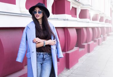 Açık hava yaşam tarzı moda sokakta yürüyen, uzun mavi ceket, hoş trendy elbise giyen genç şık kız portresi. Şehir şehir bina kamera için gülümseyen uzun siyah saçlı genç kadın 