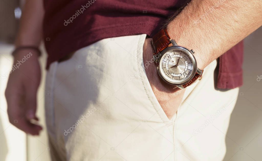 Closeup fashion image of luxury watch on wrist of man.body detail of a business man.Man's hand in bored t-shirt  in beige pants pocket closeup.Casual outfit. Tonal correction
