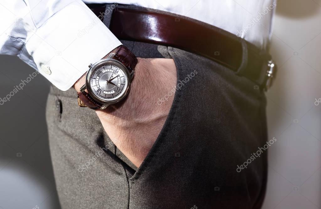 Closeup fashion image of luxury watch on wrist of man.body detail of a business man.Man's hand in a grey shirt with cufflinks in a pants pocket closeup. Tonal correction.