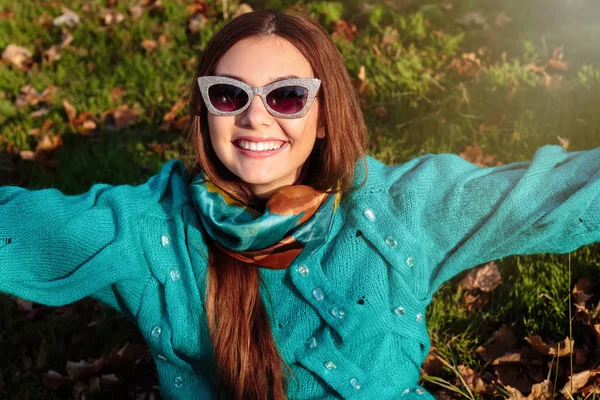 Selfie fotoğraf park yapma gülümseyen bir genç kız portresi. Genç kız güzel sonbahar yaprakları ile bir duvar backgroung bir selfie alır.