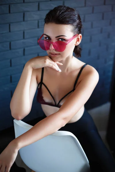 Elegante notte flash moda ritratto di moda casual alla moda giovane donna in rosa neon occhiali da sole, mutandine nere, in posa vicino a sedile muro urbano nero sulla sedia bianco.Guardando la fotocamera . — Foto Stock