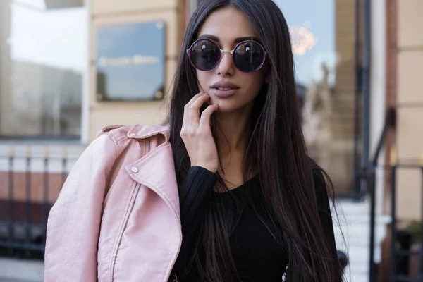 Mujer de pelo largo de moda con camisa negra y chaqueta de cuero rosa en la calle de la ciudad. Elegante chica modelo joven en ropa elegante al aire libre. Señora con maquillaje brillante.Estilo de calle de moda . — Foto de Stock