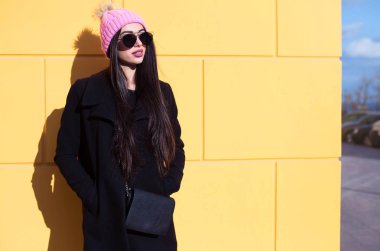 Güzel esmer kadın güneş gözlüğü ve örme kap. Mavi saçlı siyah ceket, pembe şapkalı rahat tarzı kıyafet sarı duvara poz güneş gözlüğü takıyor şık genç blogger kadın.