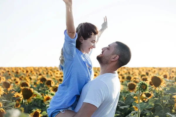 Happy woman and man in sunflower field. Cute couple  in flower field cheerful and joyful. Multiracial Asian Caucasian young couple dancing, smiling elated and serene with arms raised up.