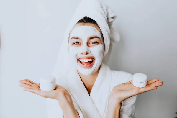 Beauty procedures skin care concept. Young woman applying facial gray mud clay mask to her face in bathroom.beautiful woman after shower with a towel on her head smiling cream on face.