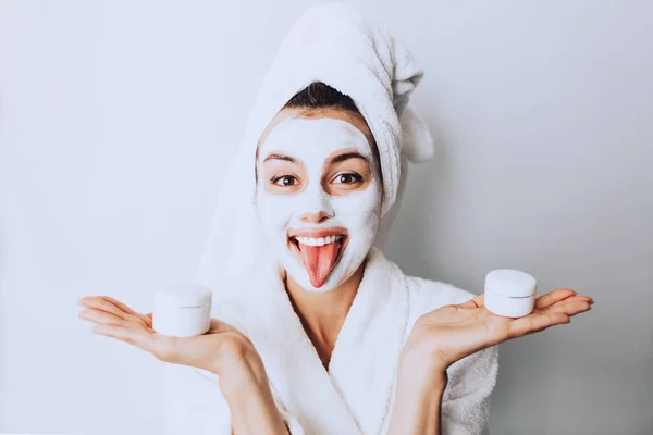 Beauty procedures skin care concept. Young woman applying facial gray mud clay mask to her face in bathroom.beautiful woman after shower with a towel on her head smiling cream on face.