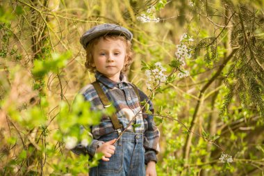 Baharda çiçek açan bahçede poz veren genç sarışın çocuk..