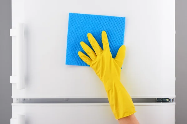 Mano en guante amarillo limpieza refrigerador blanco con trapo azul — Foto de Stock