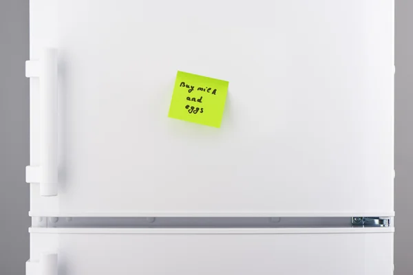 Buy milk and eggs note on green paper on refrigerator — Stock Photo, Image
