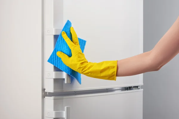 Dłoń w rękawicy żółty czyszczenia biały lodówka z blue rag — Zdjęcie stockowe