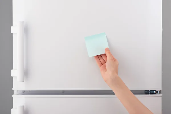 Mano femminile in possesso di carta bianca blu appiccicoso nota sul frigorifero — Foto Stock