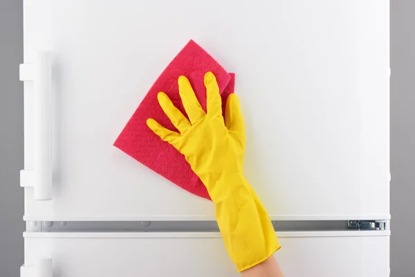 Mano en guante amarillo limpieza refrigerador con trapo rosa — Foto de Stock