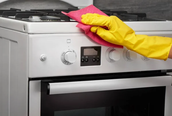 Hand in yellow glove cleaning white stove with pink rag — Stock Photo, Image