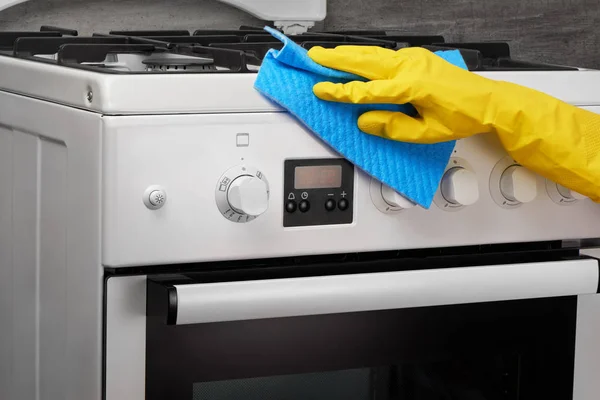 Hand in yellow glove cleaning white stove with blue rag — Stock Photo, Image