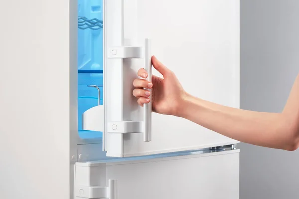 Female hand opening white refrigerator door on gray — Stock Photo, Image