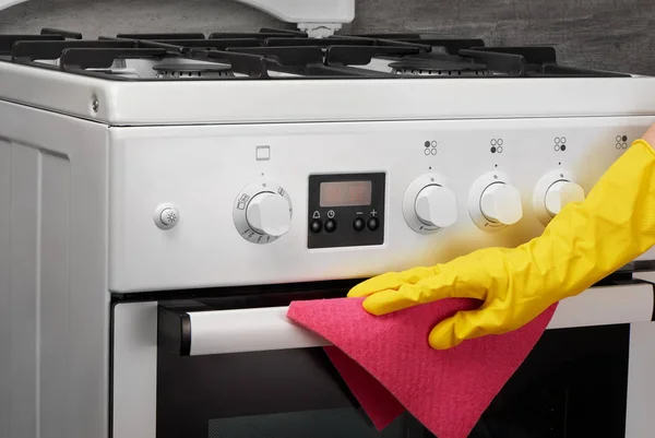 Hand in yellow glove cleaning white stove with pink rag — Stock Photo, Image