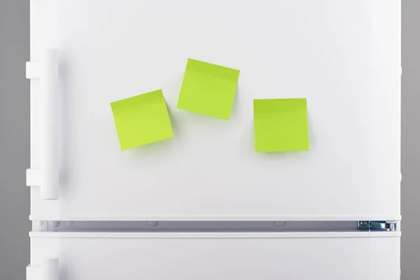 Three blank green sticky paper notes on white refrigerator — Stock Photo, Image