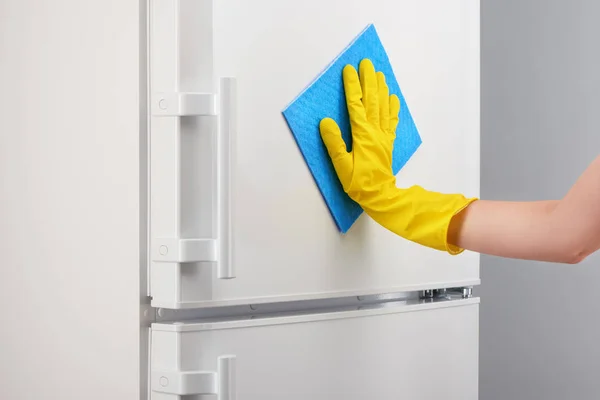 Mano en guante amarillo limpieza refrigerador blanco con trapo azul — Foto de Stock