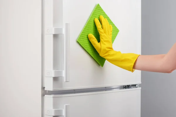Mano en guante amarillo limpieza refrigerador blanco con trapo verde — Foto de Stock