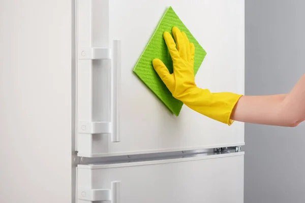 Hand in yellow glove cleaning white refrigerator with green rag — Stock Photo, Image