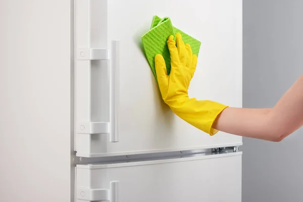 Tangan di sarung tangan kuning membersihkan kulkas putih dengan kain hijau — Stok Foto