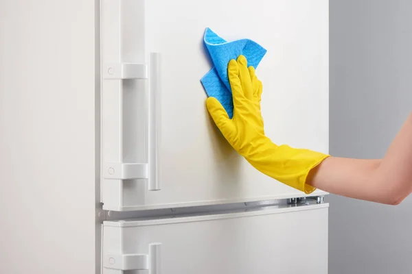 Mano en guante amarillo limpieza refrigerador blanco con trapo azul — Foto de Stock