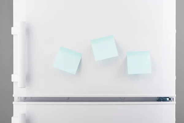 Three blank light blue sticky paper notes on white refrigerator — Stock Photo, Image