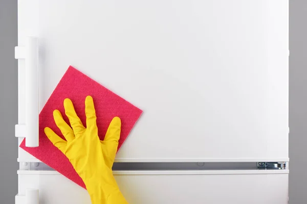 Mão em luva amarela limpeza geladeira branca com pano rosa — Fotografia de Stock