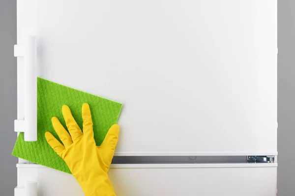 Mão em luva amarela limpeza geladeira branca com pano verde — Fotografia de Stock