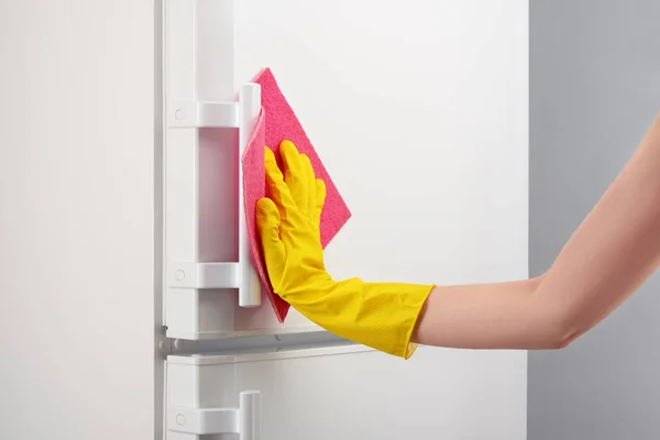 Hand in gelben Handschuh reinigt weißen Kühlschrank mit rosa Lappen — Stockfoto