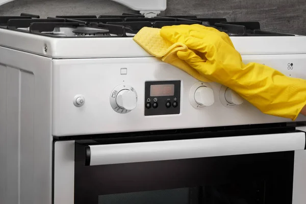 Hand in yellow glove cleaning white stove with rag — Stock Photo, Image