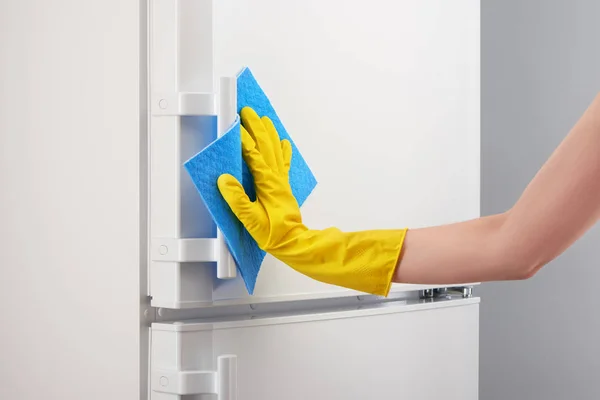 Mão em luva amarela limpeza geladeira branca com pano azul — Fotografia de Stock