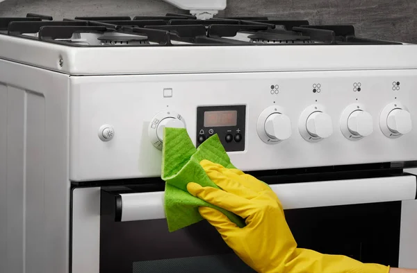 Hand in yellow glove cleaning white stove with green rag — Stock Photo, Image