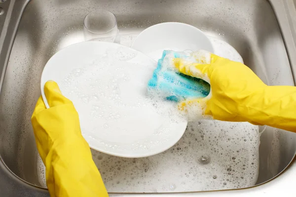 Hands in yellow gloves washing plate against kitchen sink